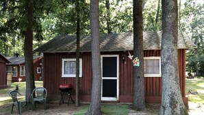 Une cabane rustique avec une seule porte et deux fenêtres, entourée d’arbres.