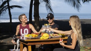 Ein Holztisch mit Speisen und Getränken, Palmen und ein Strand im Hintergrund.