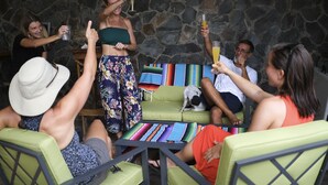 Eine Gruppe von Personen sitzt an einem Tisch, dazu eine bunte Decke, eine Steinsäule und ein Hund auf einem grünen Sofa.