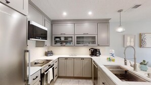 A modern kitchen with grey cabinets, a stainless steel refrigerator, a built-in oven, a microwave, a coffee maker, and a sink. - Ponce Landing 5 - Ocean front 2 bedroom townhome with garage (St. Augustine)