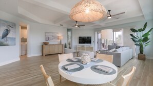 Un vaste espace de vie comprenant une table de salle à manger ronde, un ventilateur de plafond et un grand luminaire décoratif en fibres tressées.