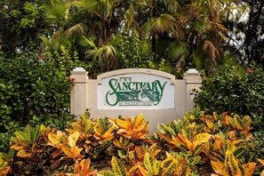Une enseigne indiquant « The Sanctuary at Wulfer Point », entourée d’une végétation luxuriante et de plantes tropicales.