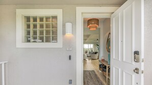 Un couloir avec une porte blanche, une fenêtre à carreaux et un luminaire en osier.