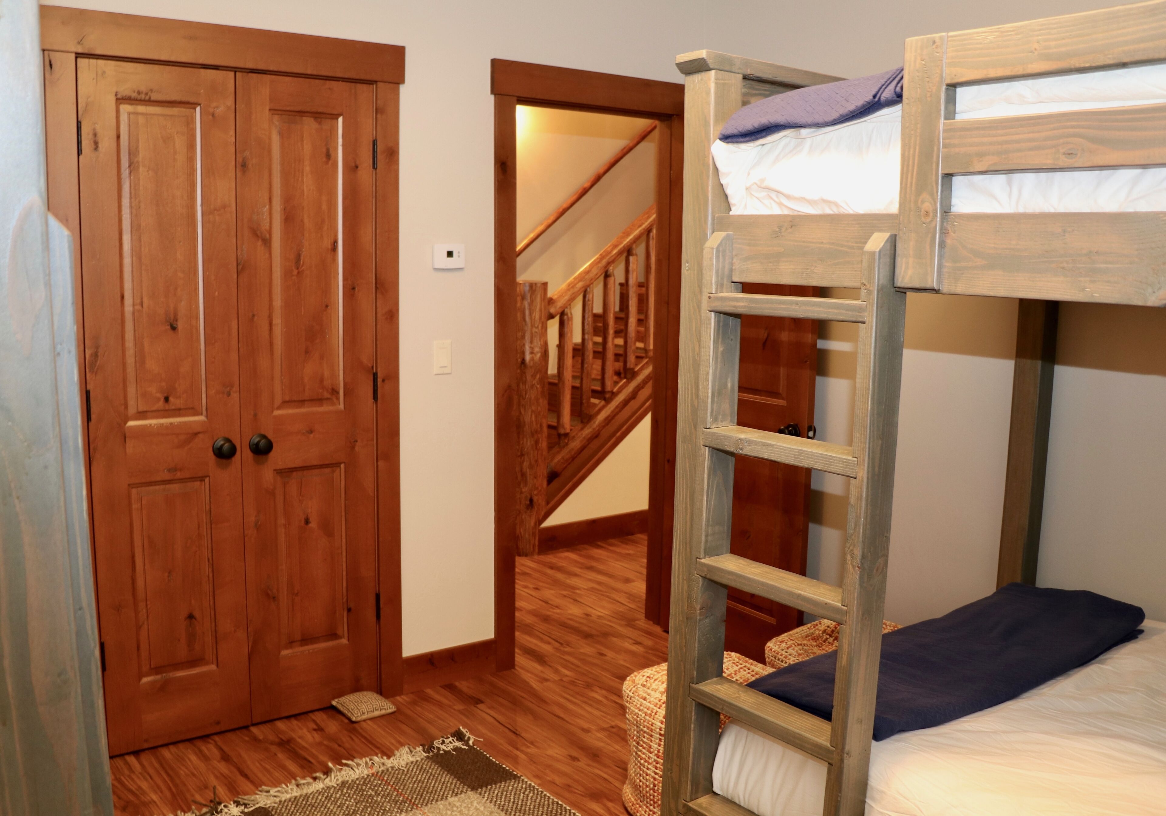 Een stapelbed met een houten ladder, een houten deur en een trap naar een andere kamer.
