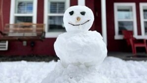Un muñeco de nieve frente a una casa roja con un porche blanco y un banco de madera.