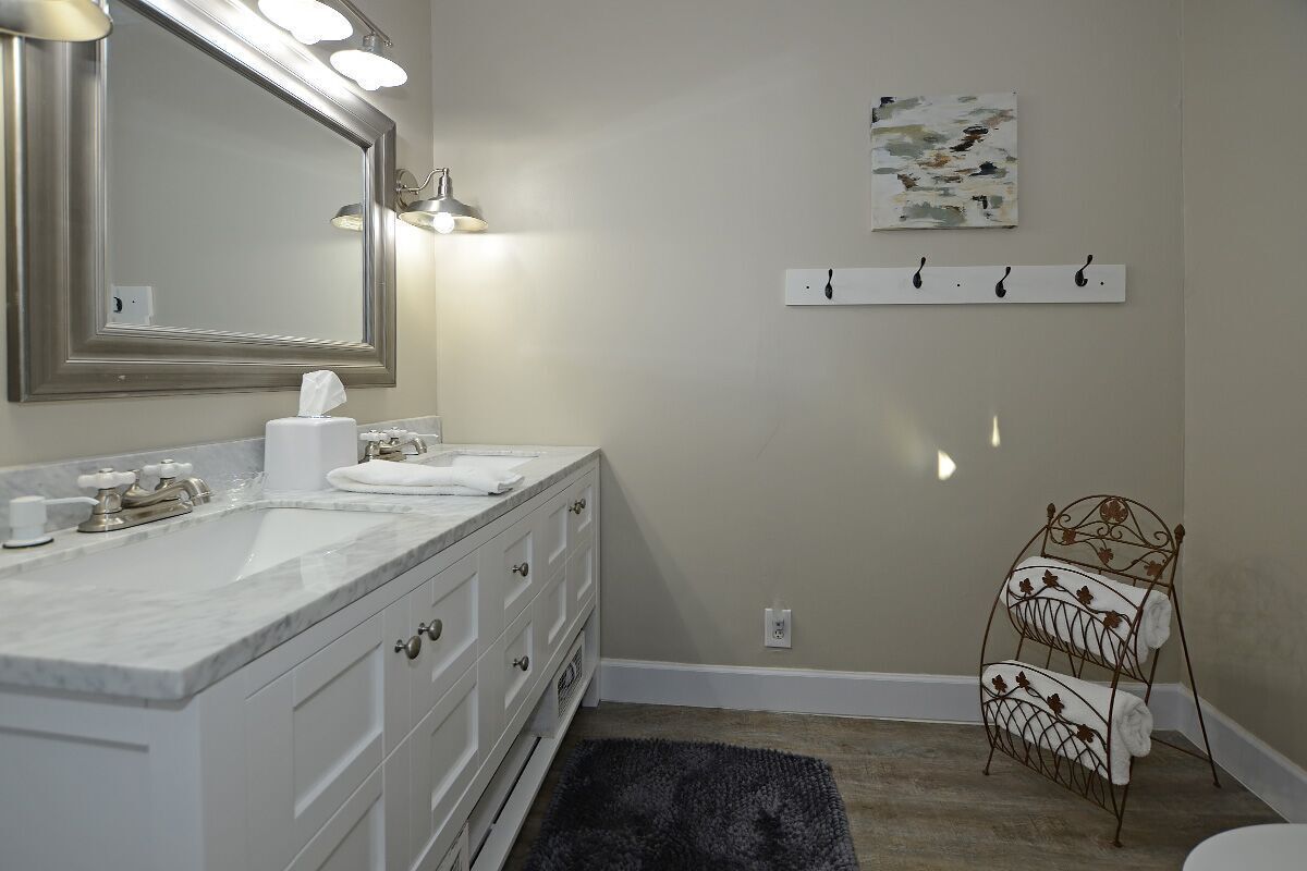 A bathroom with a large mirror, two sinks, a towel rack, and a painting on the wall.