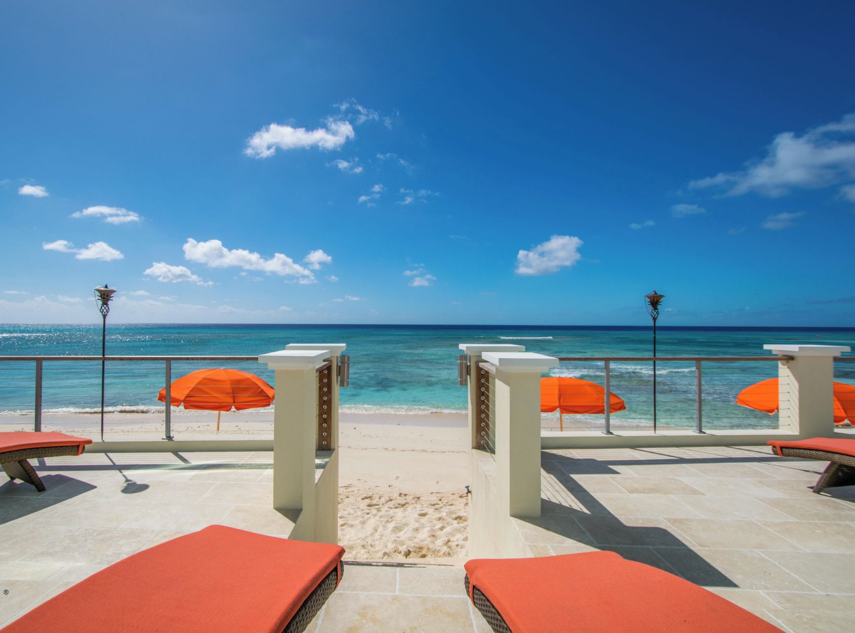 A beachside terrace with orange umbrellas, lounge chairs, and a view of the ocean.