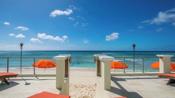 A beachside terrace with orange umbrellas, lounge chairs, and a view of the ocean.
