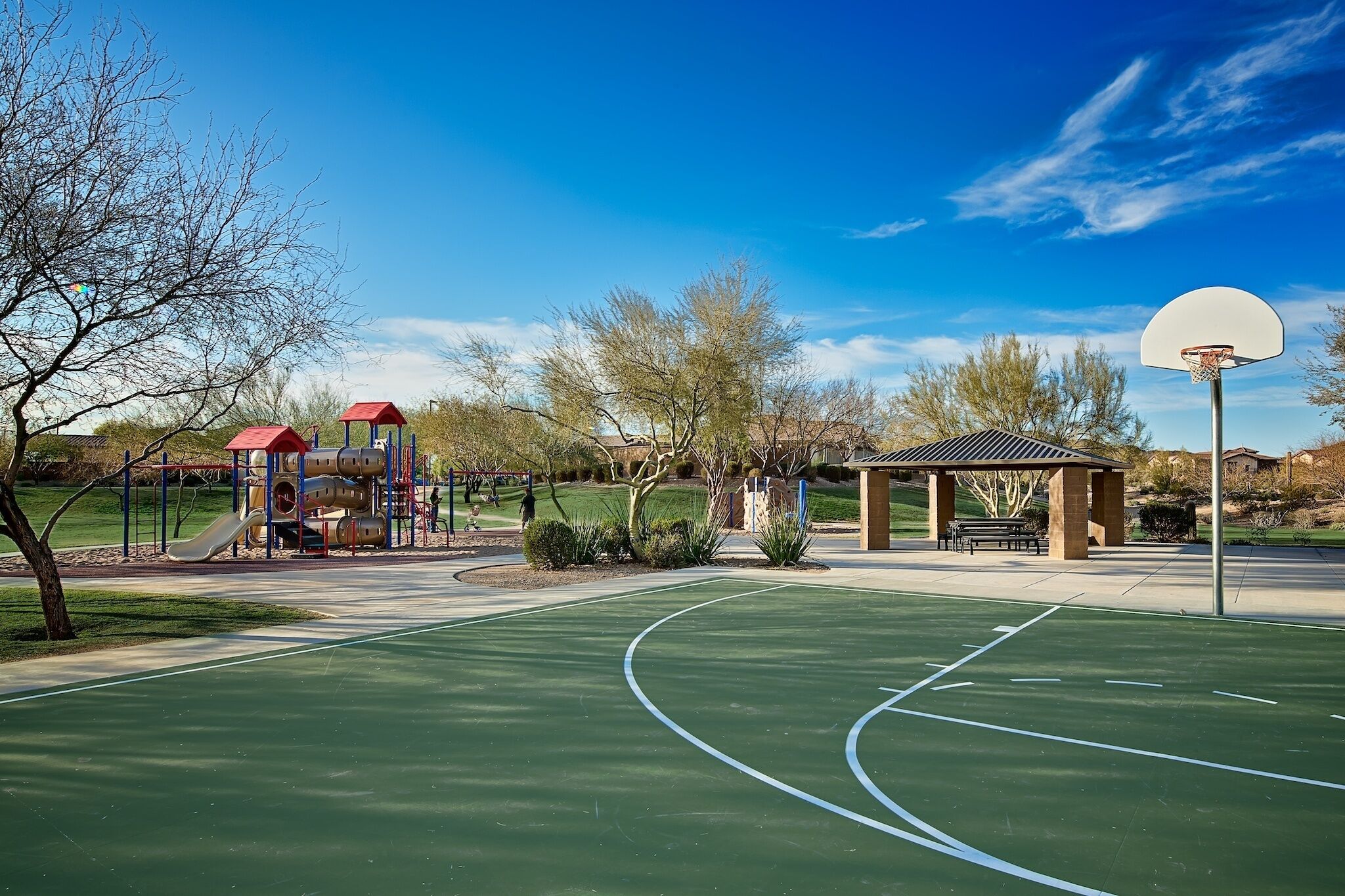 Una cancha de baloncesto con aro, un área de juegos con toboganes y un pabellón.