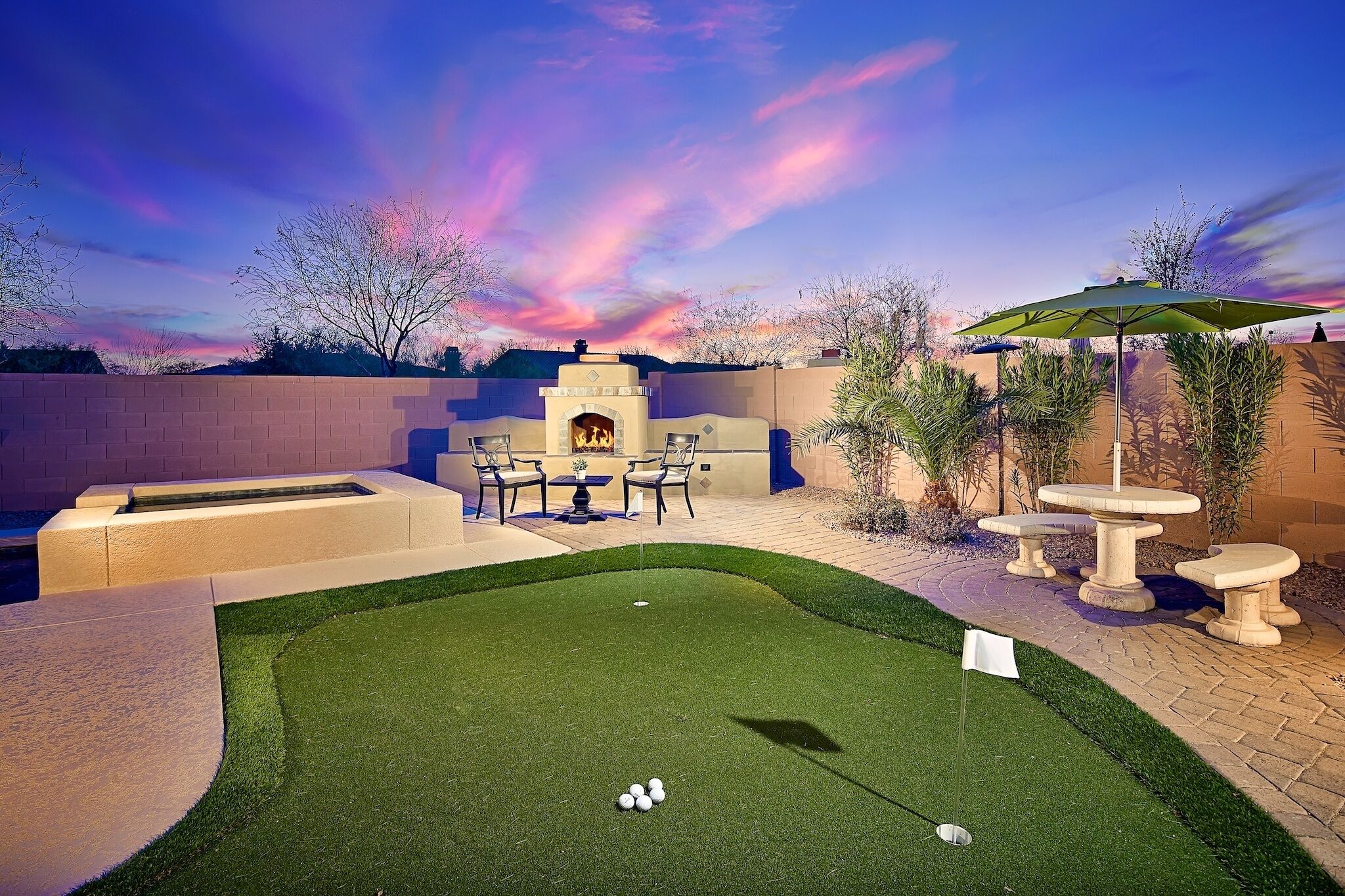 A backyard with a putting green, patio furniture, and a stone fireplace.