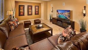 A living room with a brown leather sofa, a glass coffee table, and a television on a black stand. - Unbeatable Location, Heated Pool, 2 Primary Suites, Game Room, Hot Tub, More! (Phoenix)