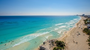 Une plage côtière aux eaux turquoise et limpides, avec un rivage sablonneux et des bâtiments qui bordent la côte.