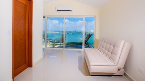 Une pièce avec un canapé blanc, une porte en bois et une vue sur la mer, visible à travers une porte vitrée.