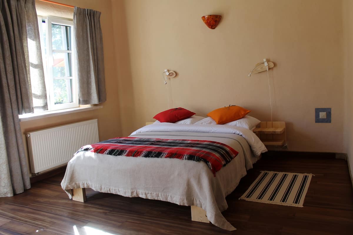 A bedroom with a bed, a radiator, a window with curtains, and a wall-mounted light fixture.
