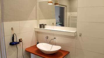 Un baño con un lavamanos blanco, un espejo encima y un perchero a la izquierda.