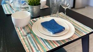 Een eettafel gedekt met borden, glazen en bestek, met een geribbelde placemat eronder.
