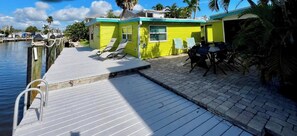 A dock with lounge chairs, a small building with a window, and a paved area.