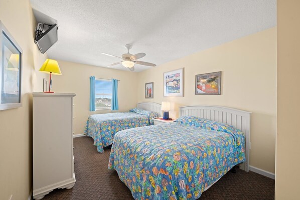 A bedroom with two beds, a ceiling fan, a window with curtains, and artwork on the walls.