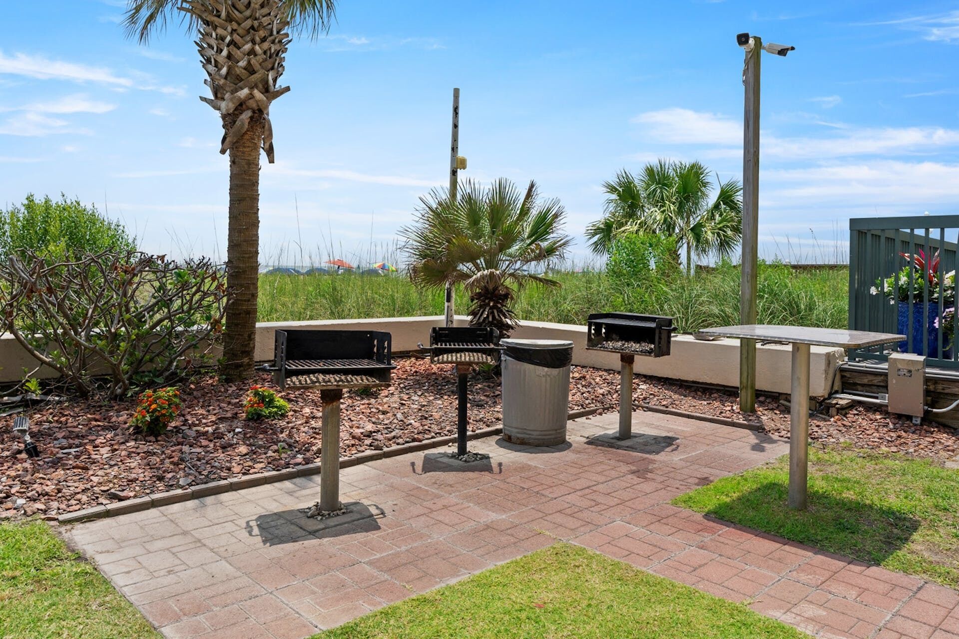 Un espace extérieur aménagé en patio, avec un barbecue, une poubelle et une caméra de surveillance.