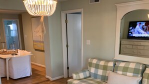 A living room with a checkered sofa, a round wicker coffee table, a chandelier, and a television on a cabinet. - Walking Distance to Ocean/Beaches, Heated/Saltwater pool-pool open 4/1-11/1 (Rehoboth Beach)