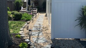 A residential backyard with a stone pathway, a white fence, and a house with a balcony. - Walking Distance to Ocean/Beaches, Heated/Saltwater pool-pool open 4/1-11/1 (Rehoboth Beach)