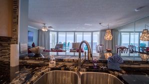 A modern kitchen with a large island, a dining area with chairs, and a view of the ocean through large windows.