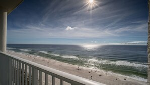 A beach view from a balcony with a railing, ocean waves, and a clear sky.