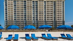 A multi-story hotel with balconies, a beachside location, and blue sun loungers with umbrellas.