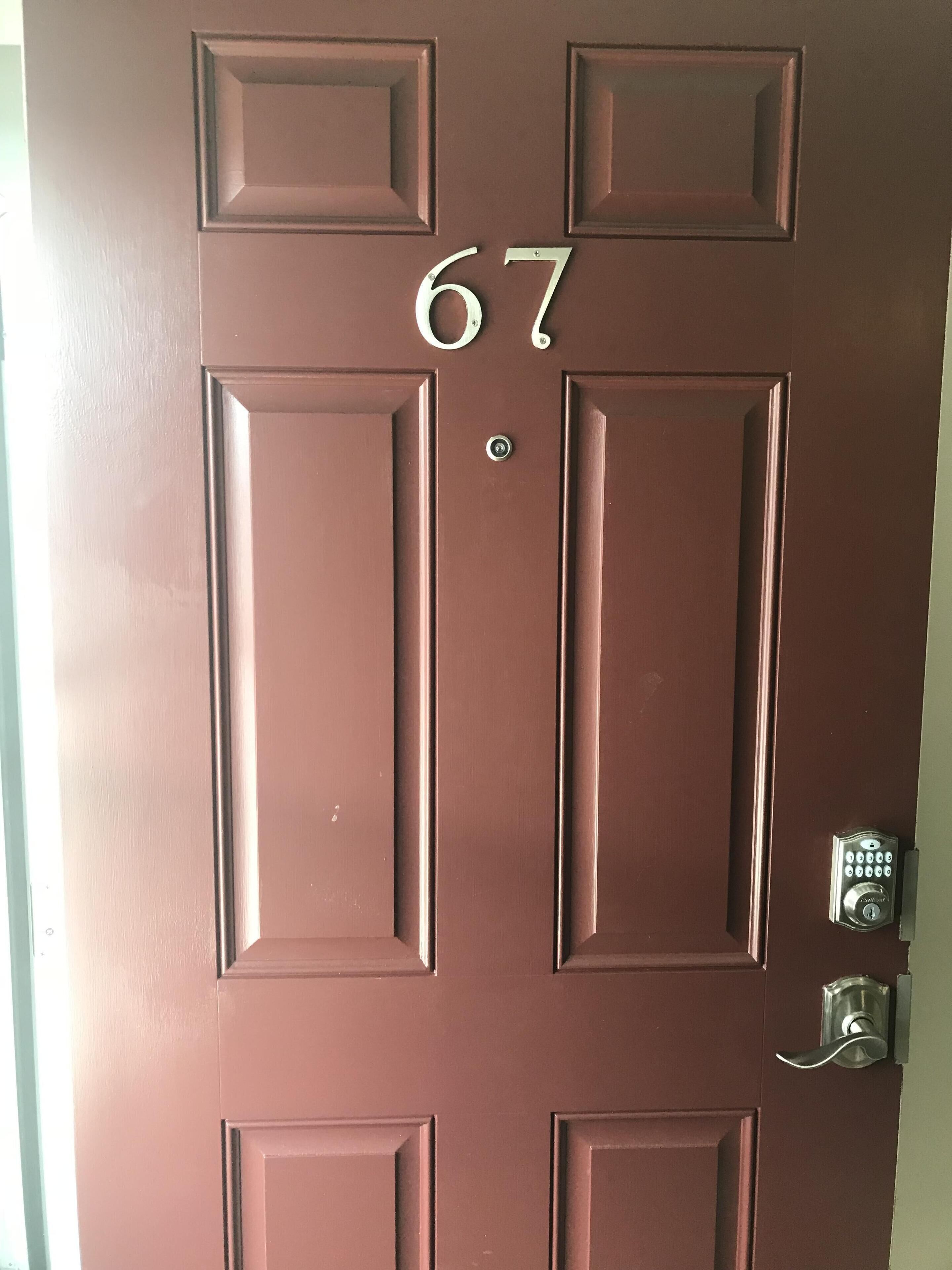 A brown door with the number 67, a keyhole, and a doorbell.