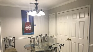 A dining area with a glass table surrounded by four chairs, a chandelier, and a door with a decorative panel. - Road Dawg Condo  Welcome to God's country.  (Starkville)