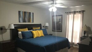 A bedroom with a bed, two bedside tables, a ceiling fan, and a window with curtains. - Road Dawg Condo  Welcome to God's country.  (Starkville)