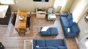 A modern living room with a sofa, a dining table, a TV, and a small side table. - 3BR Waterfront Home Fishing Boating Views (Stacy)