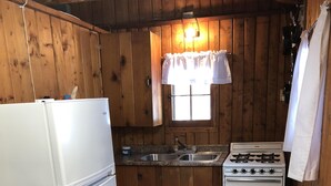 Ett kompakt kök med träpanel på väggarna, ett vitt kylskåp, en spis och ett handfat.