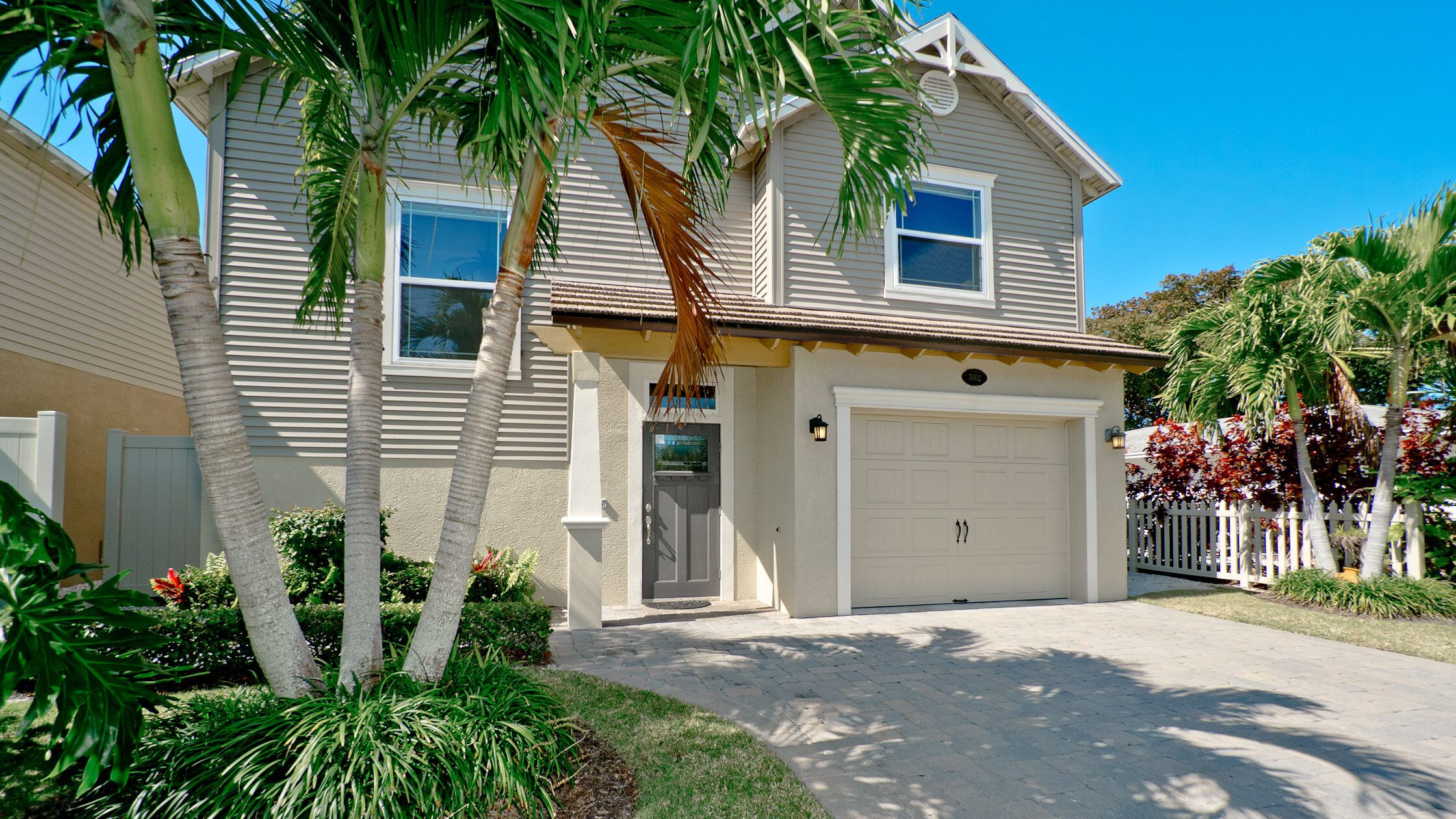 A two-story house with a garage, surrounded by palm trees and a well-maintained lawn.