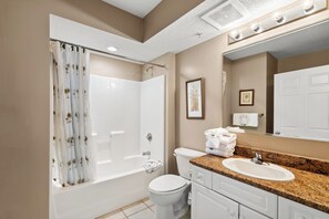 A bathroom with a bathtub, toilet, sink, and a shower curtain with palm tree patterns.