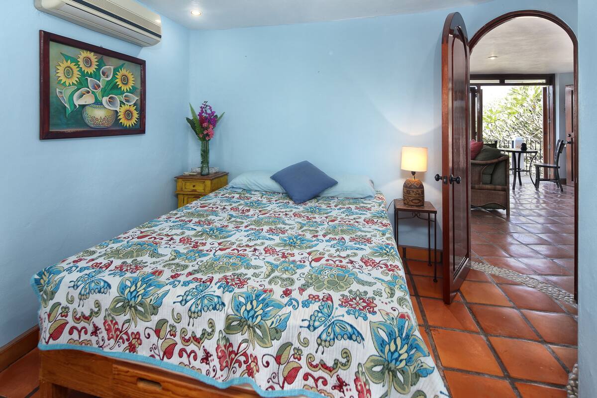 Une chambre à coucher avec une couvre-lit à motifs floraux, une table de chevet avec une lampe et un tableau représentant des tournesols.