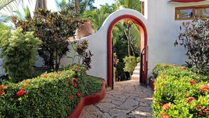 A pathway leading to a building with a red archway, surrounded by lush greenery and flowering plants. - Caracol Estates (Sayulita)