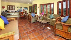 A spacious living area with a kitchen, wooden furniture, and large windows offering a view of the outdoors. - Caracol Estates (Sayulita)