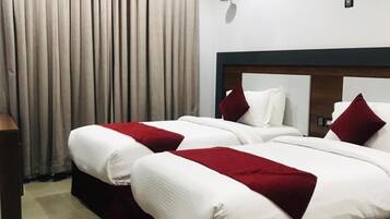 Habitación de hotel con cama doble, mesita de noche, lámpara y ventana con cortinas.