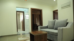 A living room with a grey sofa, a wooden coffee table, and patterned rugs. - Nizwa Residence Hotel Apartment (Nizwa)