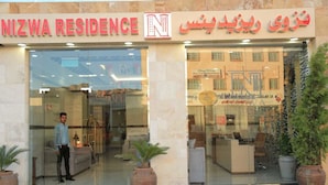 A hotel entrance with a reception desk, a man standing by the entrance, and potted plants. - Nizwa Residence Hotel Apartment (Nizwa)