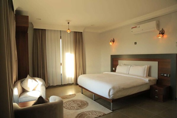 Habitación de hotel con cama, una silla, mesita de noche, equipo de aire acondicionado y ventana con cortinas.