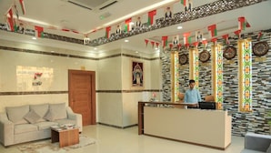 A hotel reception area with a receptionist, a sofa, a coffee table, and a patterned wall with clocks. - Nizwa Residence Hotel Apartment (Nizwa)