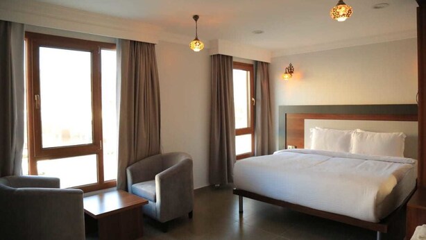 A hotel room with a bed, two armchairs, a small table, and a window with curtains. - Nizwa Residence Hotel Apartment (Nizwa)
