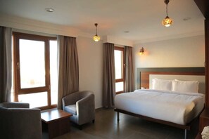 Habitación de hotel con una cama, dos sillones, una mesita y una ventana con cortinas.