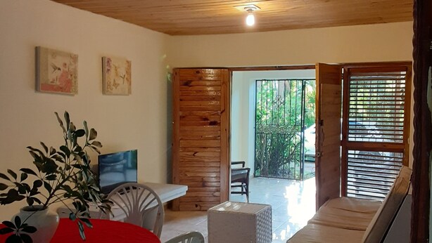 A cozy room with a wooden ceiling, a dining table with chairs, a sofa, and a TV.