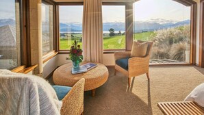 Una habitación con un gran ventanal que ofrece vistas a la montaña, una silla de mimbre, una mesa redonda con un florero y un ambiente acogedor.