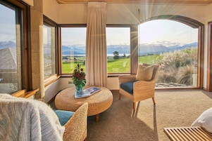 Una habitación con un gran ventanal que ofrece vistas a la montaña, una silla de mimbre, una mesa redonda con un florero y un ambiente acogedor.