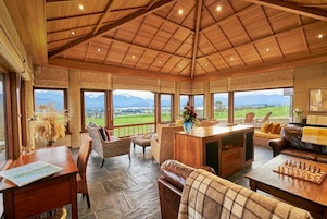 Amplia habitación con techo alto, ventanas grandes que ofrecen vistas a la montaña, un escritorio de madera y cómodas zonas de estar.