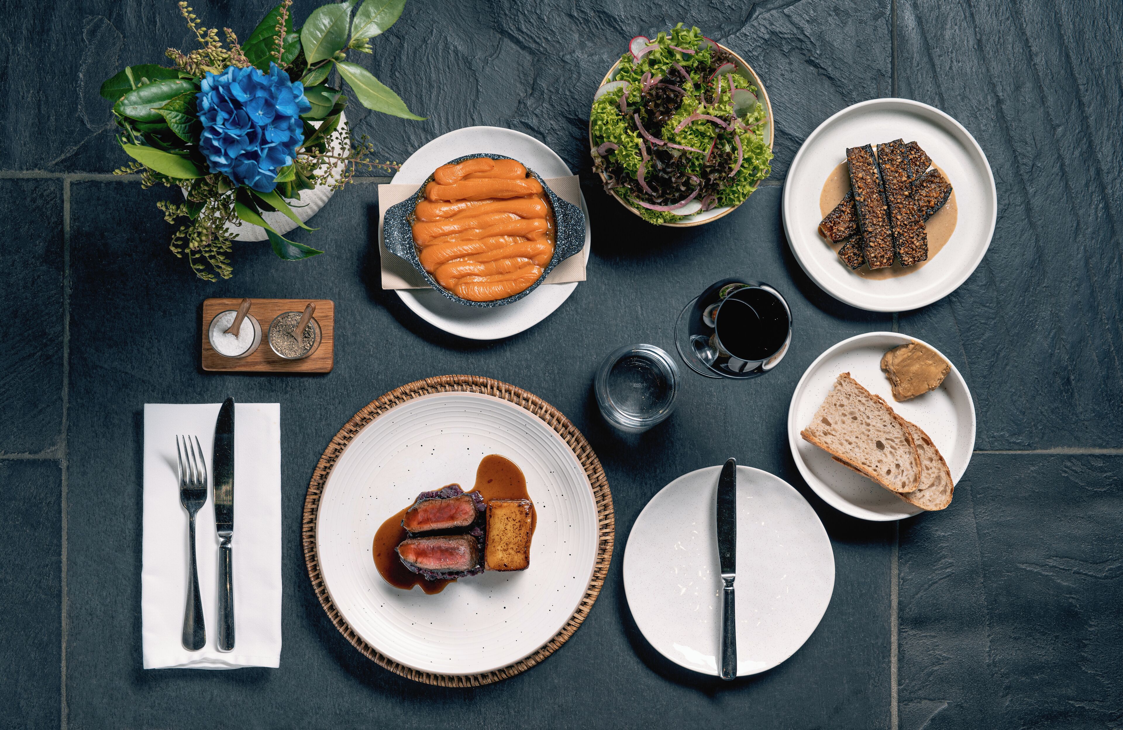 Una mesa servida con diversos platos, entre ellos un tazón de sopa, un plato de carne y un bol de ensalada.